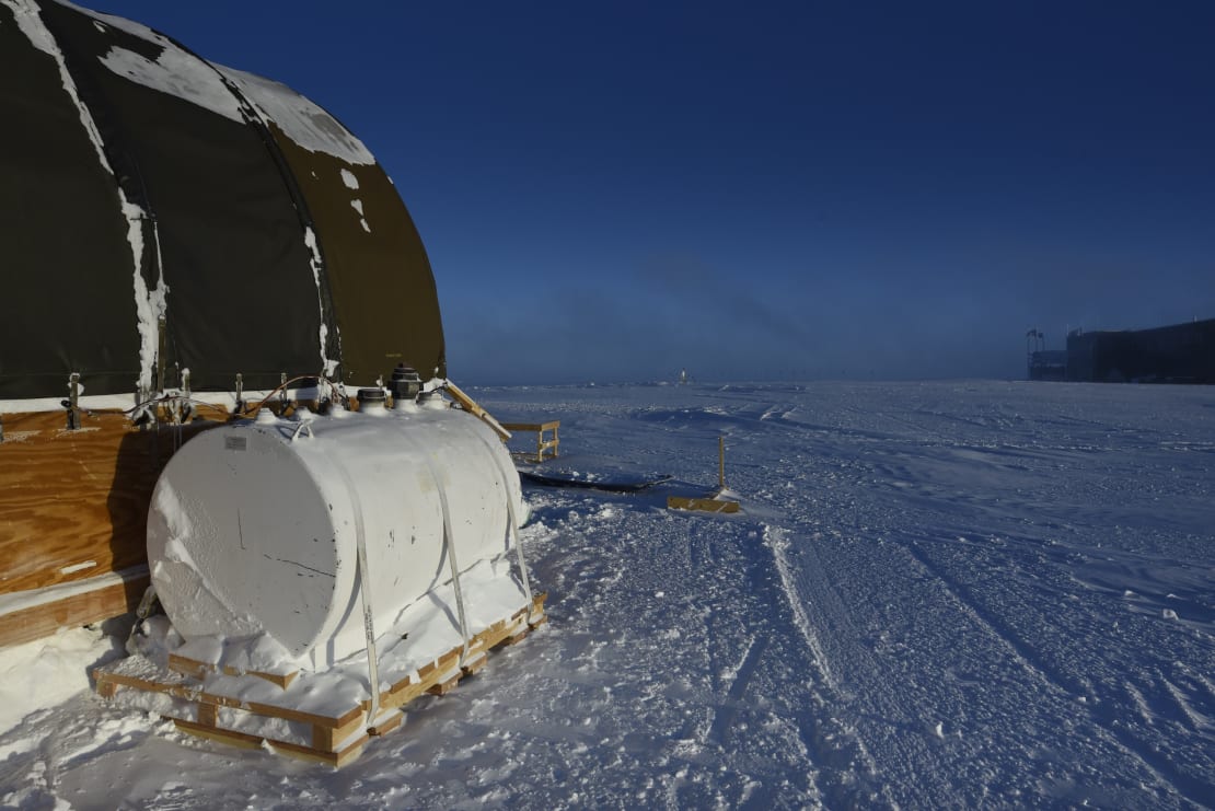 A fuel barn off to the left, the edge of the South Pole station in the distance off to the right.