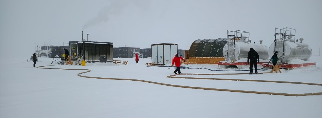 View of several people out on the ice working on a fuel hose.