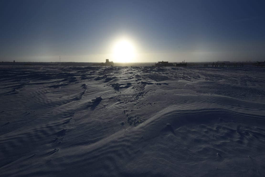 A bright sun “sitting” on the horizon at the South Pole, with the foreground dark and shadowy.